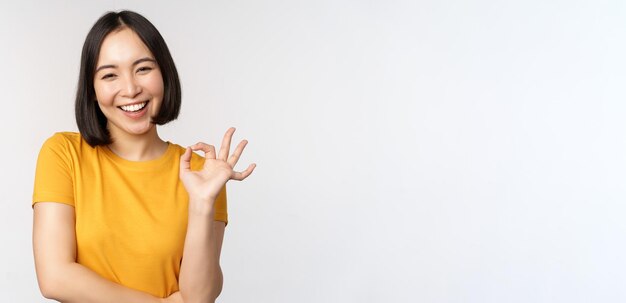 Beautiful young woman showing okay sign smiling pleased recommending smth approve like product stand