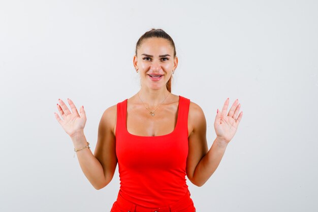 Beautiful young woman showing surrender gesture in red tank top and looking cheery. front view.