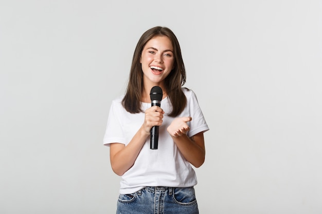 Красивая молодая женщина поет песню в микрофон в караоке, стоя на белом.