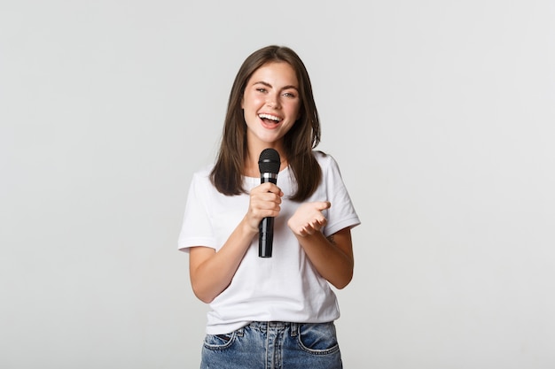 Beautiful young woman singing song in microphone at karaoke, standing white.