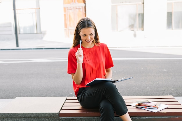 Beautiful young woman sitting on bench reading diary