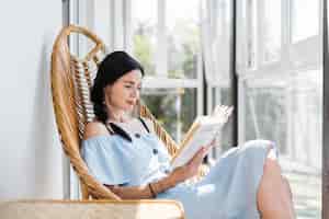 Free photo beautiful young woman sitting on chair reading book