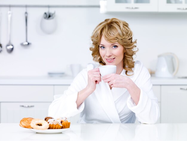 Beautiful young woman sitting in the kitchen and drinking coffee - indoors