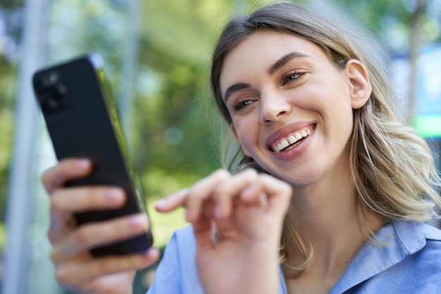 Bella giovane donna che si siede all'aperto sulla via che sorride allo smartphone che compra ordine online sul cellulare