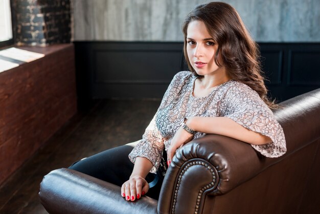 Beautiful young woman sitting on sofa looking at camera