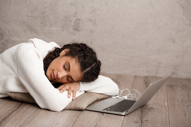 Foto gratuita bella giovane donna che dorme sul cuscino al piano vicino al computer portatile