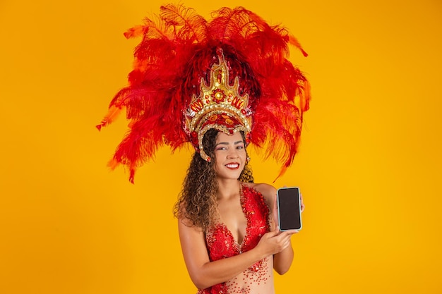 Beautiful young woman in special carnival feather costume holding a smartphone with blank screen with space for text. virtual carnival, promotion and advertisements Premium Photo