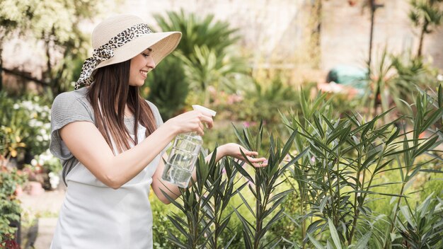 成長している植物にボトルから水を噴霧する美しい若い女性