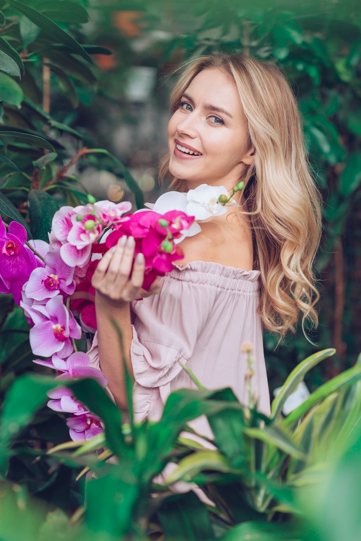 免費 Photo 一位漂亮的年轻女人站在植物附近,手里拿着兰花的树枝