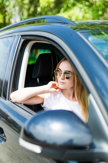 Beautiful young woman in sunglasses driving her car