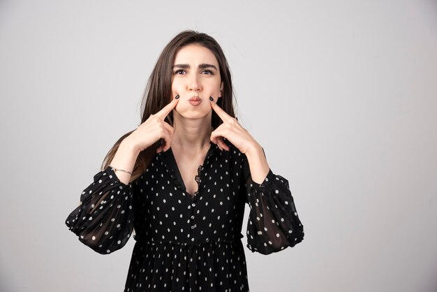 Beautiful young woman touching her cheeks and standing against grey background.