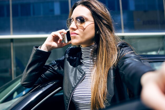 Beautiful young woman using her mobile phone in the car.