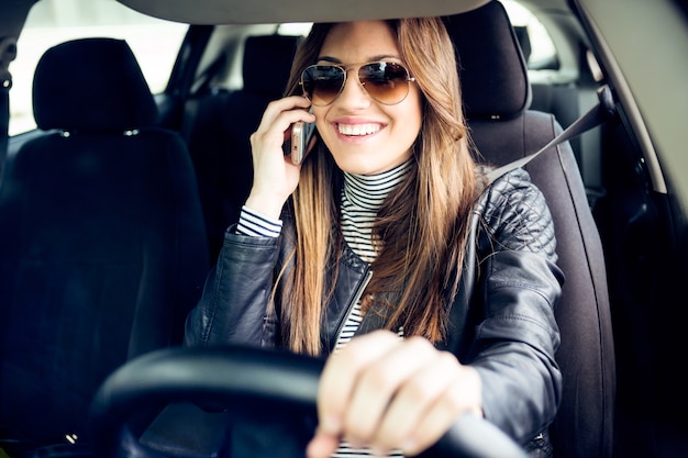 彼女の携帯電話を車で使っている美しい若い女性。