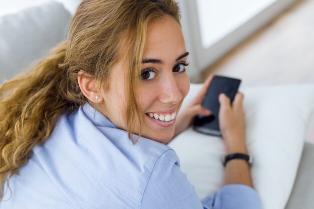 아름 다운 젊은 여자 집에서 그녀의 휴대 전화를 사용 하여.