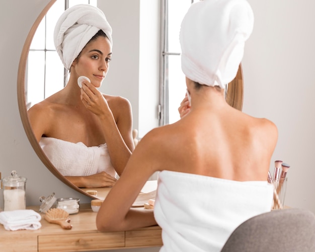 Free photo beautiful young woman using products and looking into the mirror