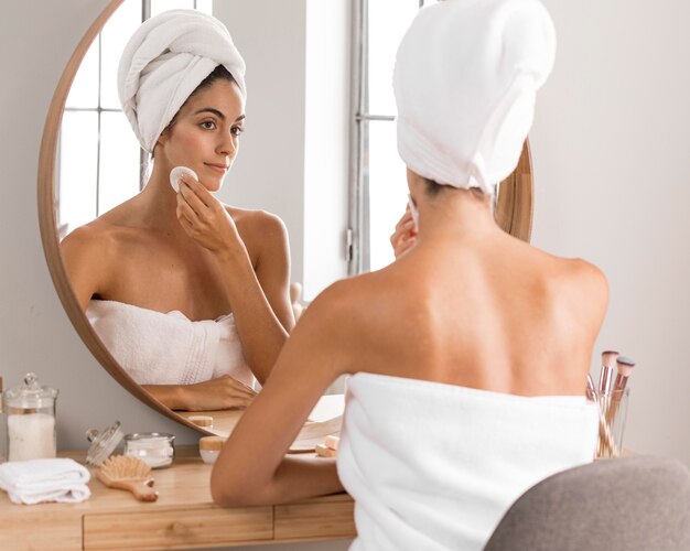 Beautiful young woman using products and looking into the mirror