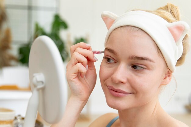 Beautiful young woman using tweezers on her brows