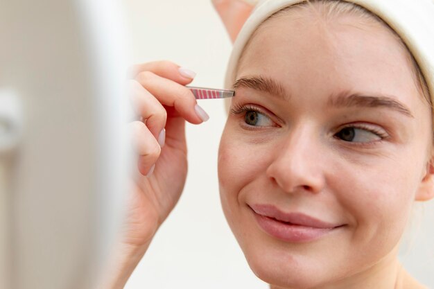 Beautiful young woman using tweezers on her brows