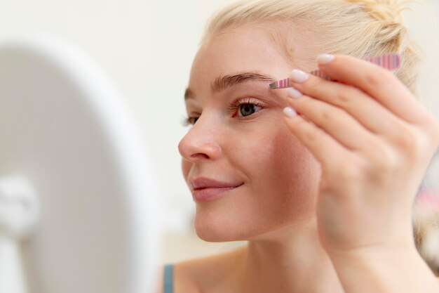 Beautiful young woman using tweezers on her brows