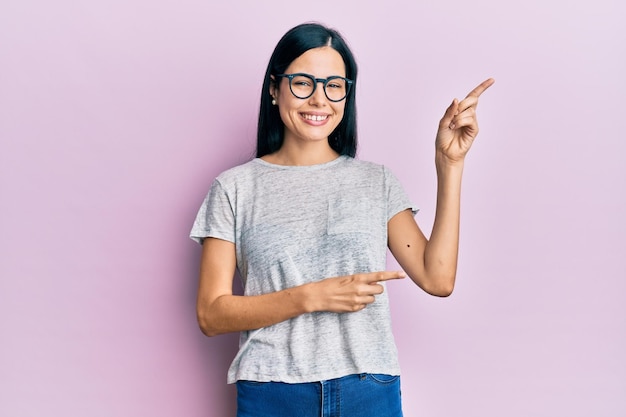 Free photo beautiful young woman wearing casual clothes and glasses smiling and looking at the camera pointing with two hands and fingers to the side