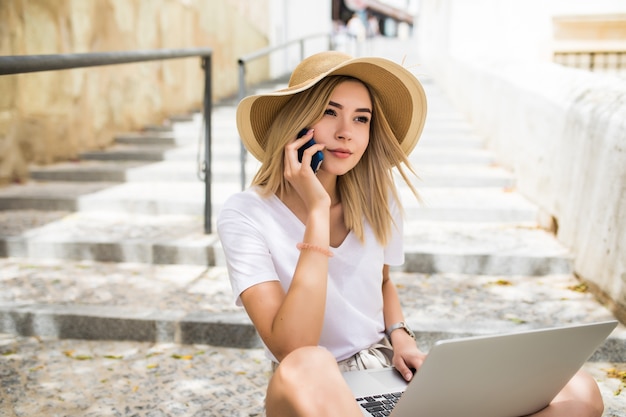 Beautiful young woman wearing casual summer outfit sitting on street stairs