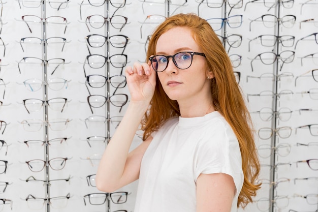 Eyeglasses красивой молодой женщины нося смотря камеру в магазине оптика