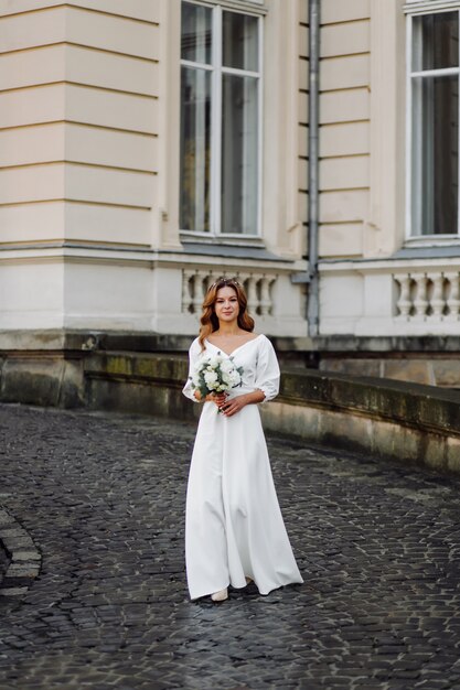 Красивая молодая женщина в свадебном платье позирует на улице в городе