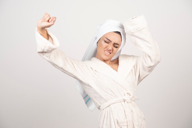 Beautiful young woman in a white bathrobe posing on a white wall .