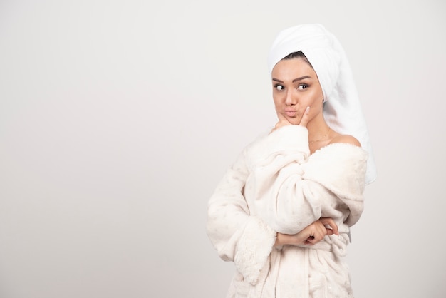 Beautiful young woman in a white bathrobe posing on a white wall