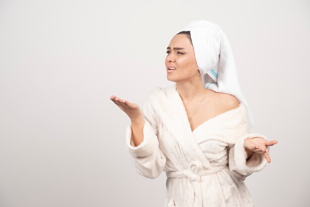 Beautiful young woman in a white bathrobe posing on a white wall