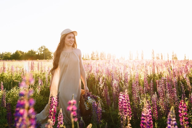 beautiful young woman in white dress and straw hat walking in flower field