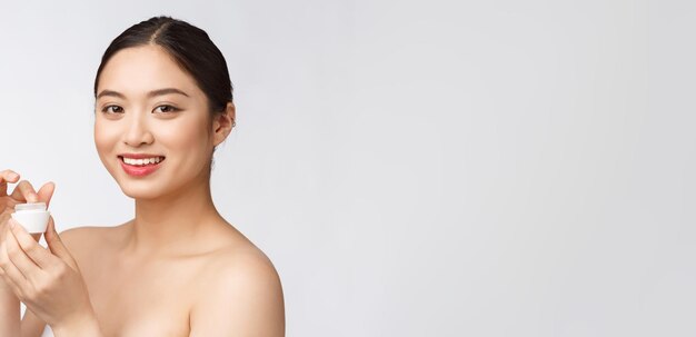 Красивая молодая женщина на белом изолированном фоне с косметическим кремом для лица азиатка