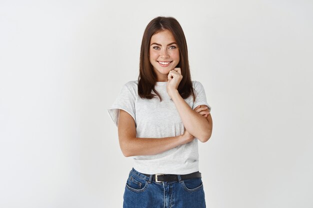 Beautiful young woman in a white t-shirt on a white wall.