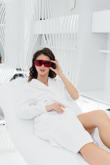 A beautiful young woman will undergo laser hair removal with modern equipment in a spa salon.
