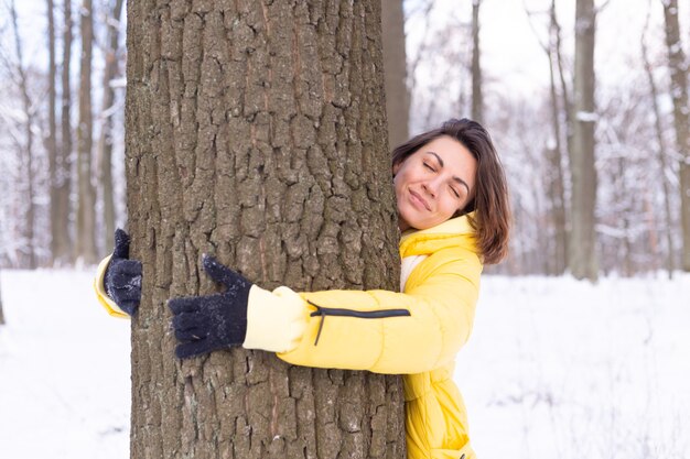 Beautiful young woman in the winter forest shows tender feelings for nature, shows her love for the tree
