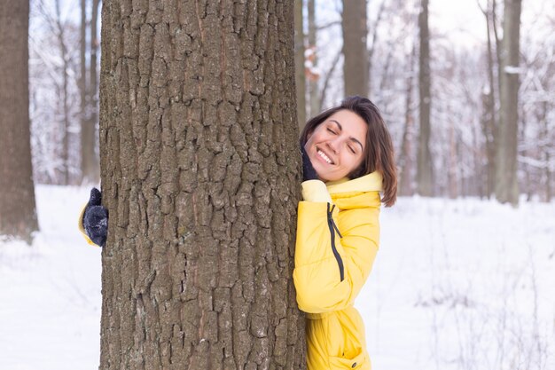 겨울 숲에서 아름 다운 젊은 여자는 자연에 대한 부드러운 감정을 보여주고 나무에 대한 그녀의 사랑을 보여줍니다