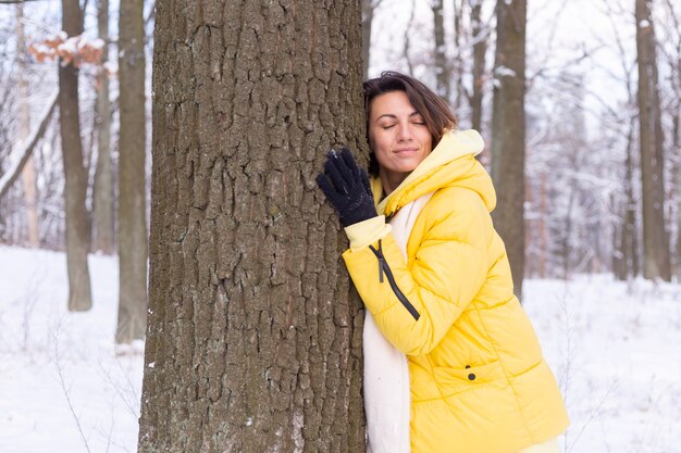 Beautiful young woman in the winter forest shows tender feelings for nature, shows her love for the tree