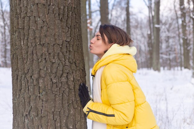 Beautiful young woman in the winter forest shows tender feelings for nature, shows her love for the tree