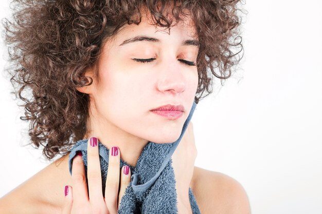 Beautiful young woman wiping her face with napkin against white background