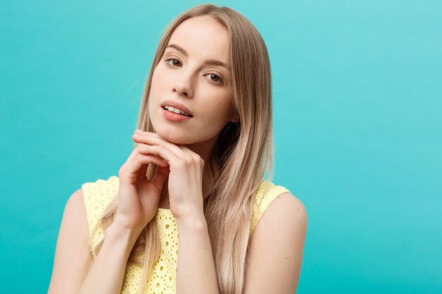 Beautiful young woman with clean perfect skin. Portrait of beauty model touching her face. Spa, skincare and wellness. Close up, blue background, copyspace.