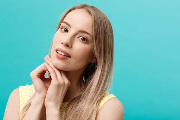 Beautiful young woman with clean perfect skin. Portrait of beauty model touching her face. Spa, skincare and wellness. Close up, blue background, copyspace.