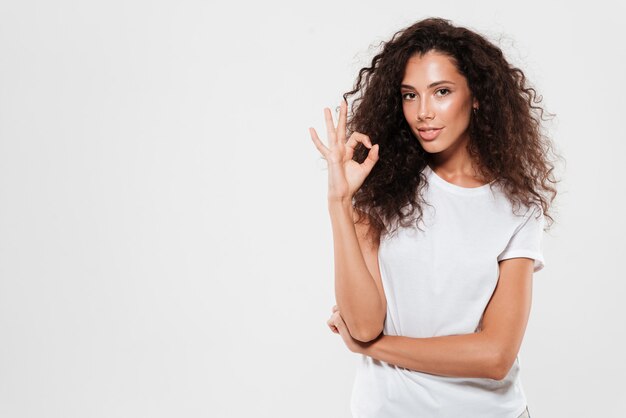 Beautiful young woman with curly hair showing ok