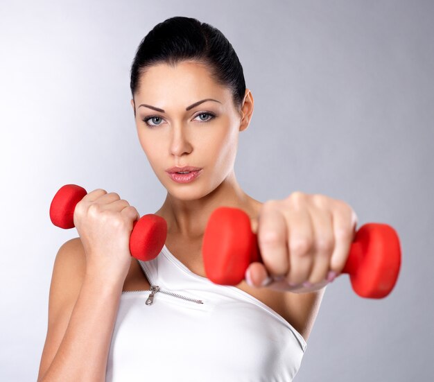 Beautiful young woman with dumbbells -  grey studio space. Healthy lifestyle concept.