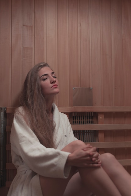 Beautiful young woman with eye closed relaxing in wooden sauna