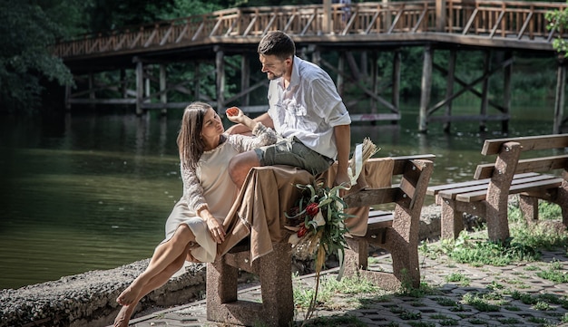 A beautiful young woman with flowers and her husband are sitting on a bench and enjoying communication, a date in nature, romance in marriage.