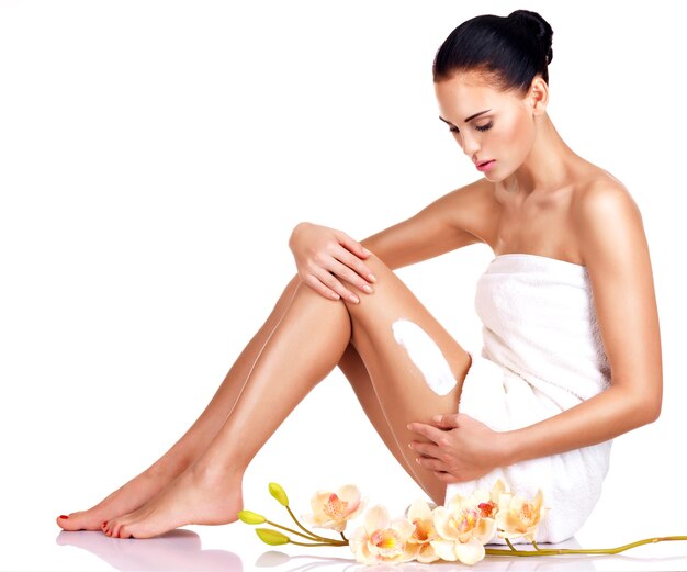 Beautiful young woman with flowers using the cream.