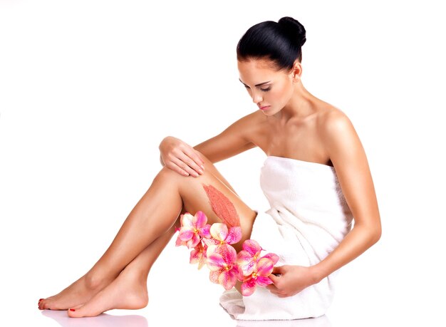 Beautiful young woman with flowers using a scrub. isolated on white