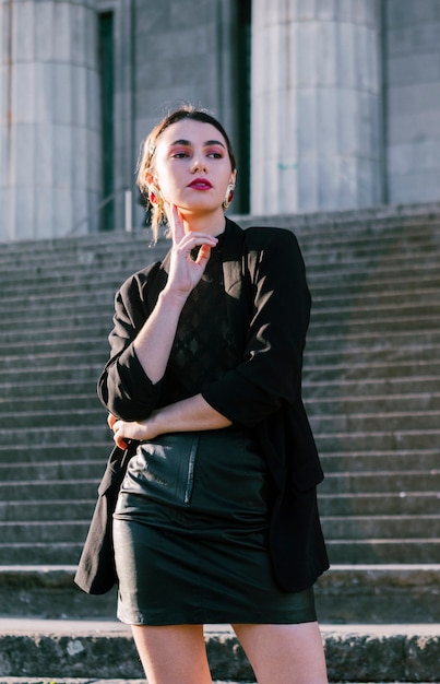 Beautiful young woman with hand on her chin standing in front of staircases