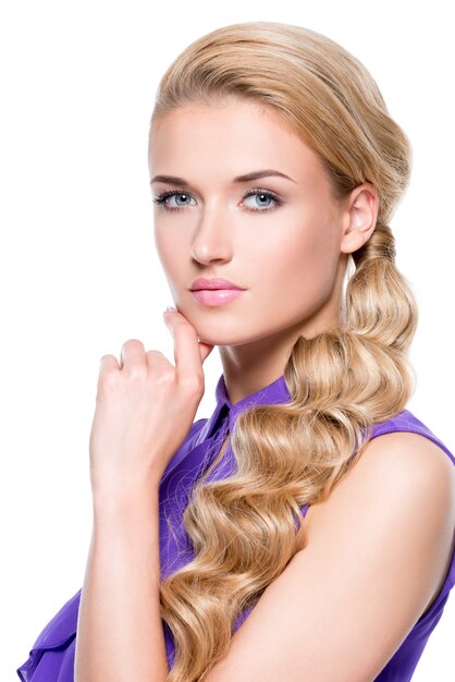 Beautiful young woman with hand near face. Fashion model with long blond curly hair. Isolated on white wall.