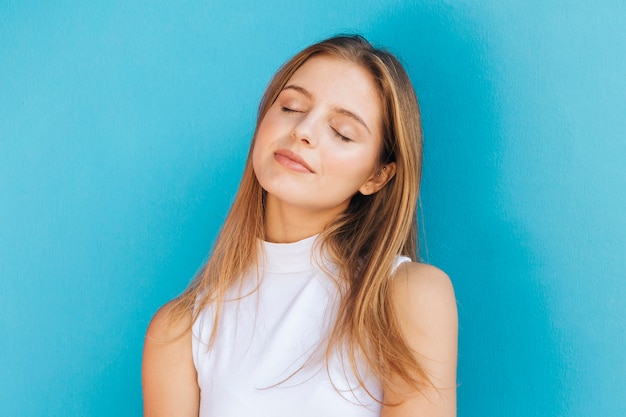 Free photo beautiful young woman with her eye closed against blue backdrop